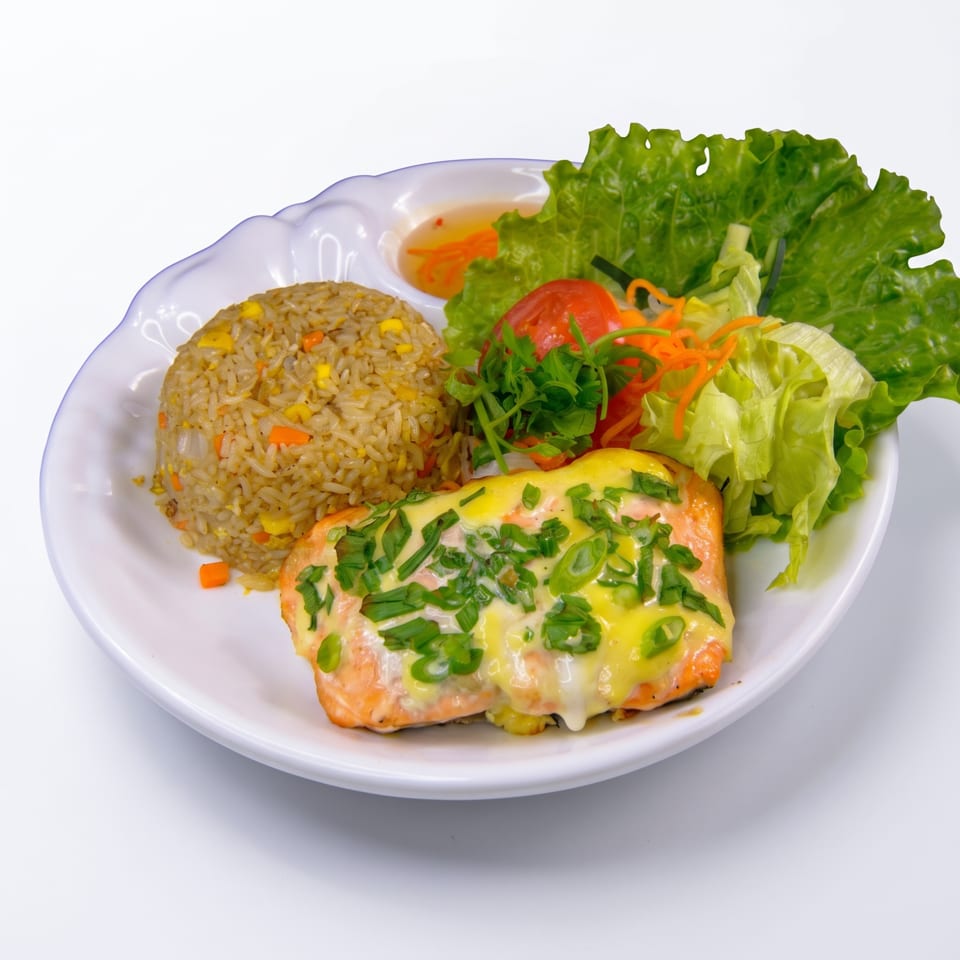 Grilled salmon topped with creamy sauce and green onions, served with vegetable rice, salad, and dipping sauce.